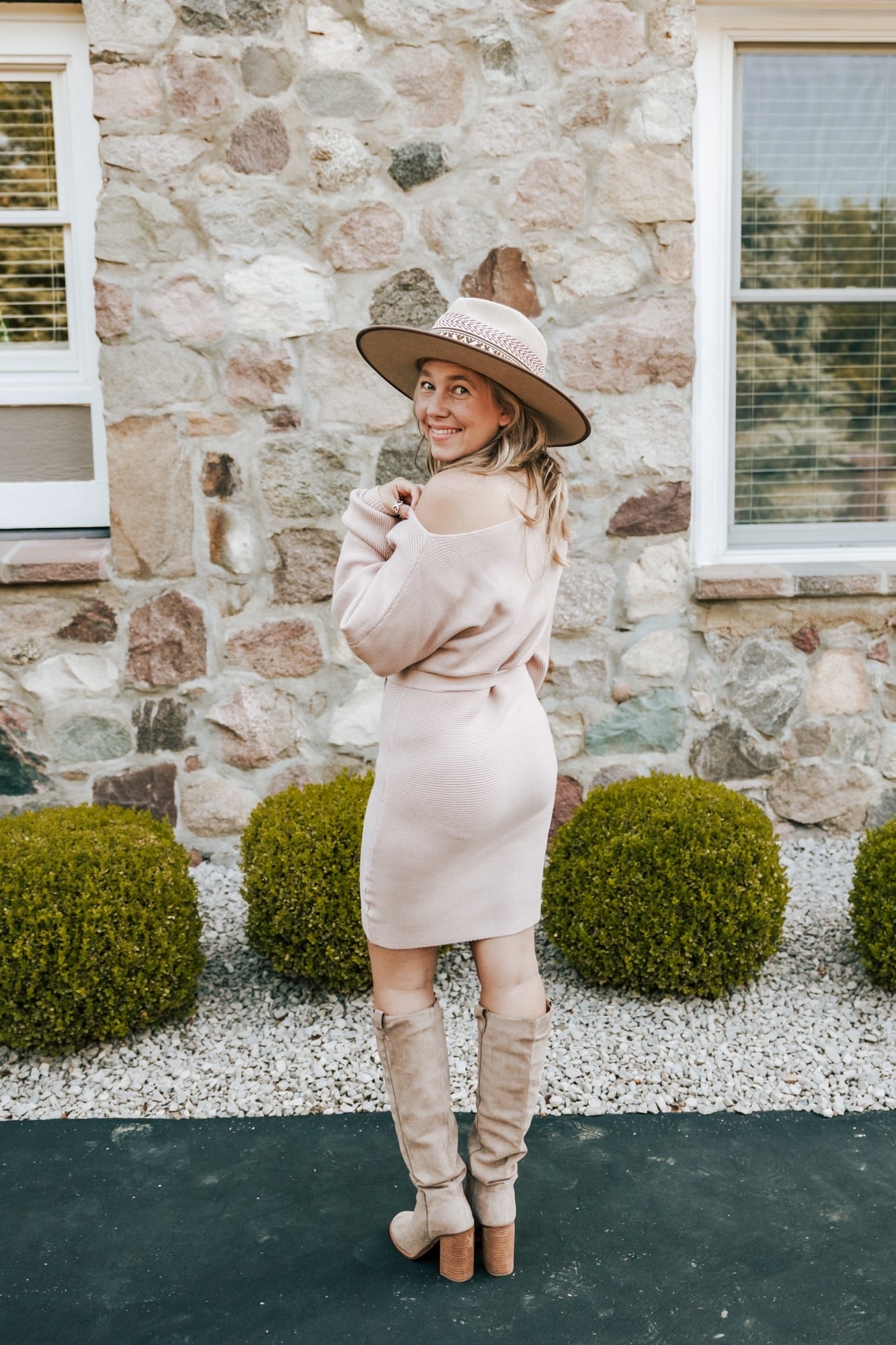 Woman in a pink dress and beige hat standing in front of a stone building.